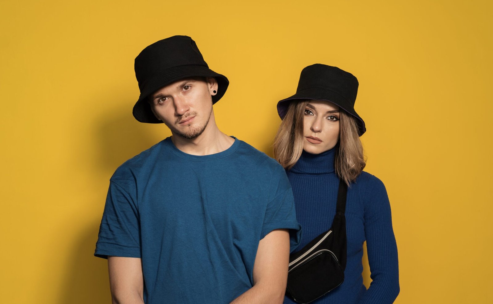 Portrait young pretty man and woman in blue t-shirts and black caps posing on yellow background