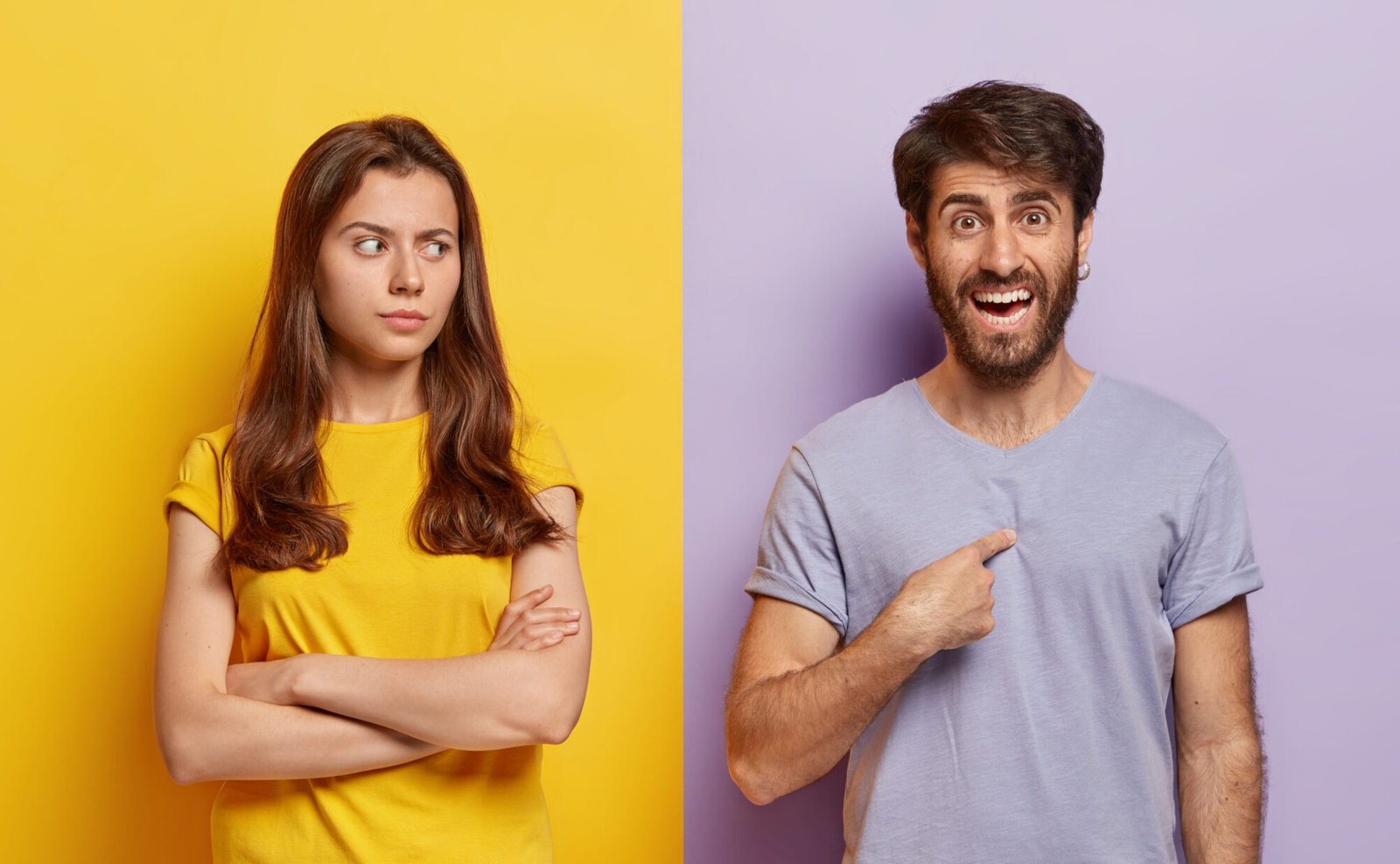 Studio shot of pleased smiling millennial man points at himself, asks why him, angry sad woman keeps arms folded, looks in dissatisfaction at boyfriend, suspects in something. People, emotions concept