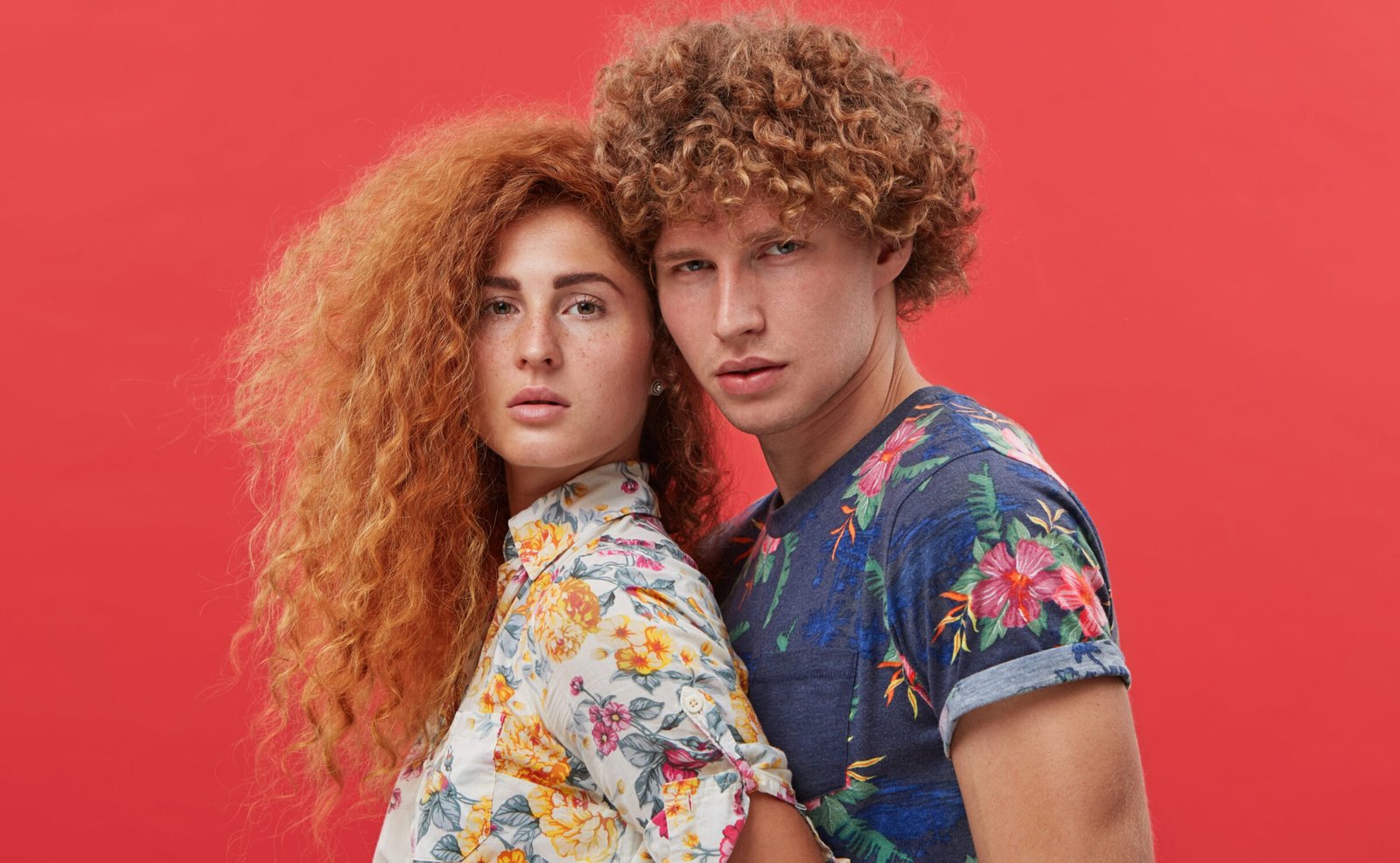 Fashion, clothing design, style and advertisement concept. Picture of two good-looking young people of European appearance modeling during photo shooting in studio, standing close to each other
